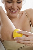 Junge Frau reibt sich den Ellbogen mit Zitronenhälfte ein
