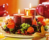 Kerzen auf Teller in Kranz aus Physalis und Früchten
