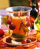 Glass windlight with orange candle, with ornamental apples