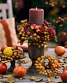 A burning candle on a table with autumn decorations