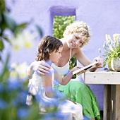 Frau und Kind lesen beim Gartentisch