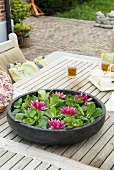 Seerosenblüten und Schwimmpflanzen in Wasserschale auf Gartentisch
