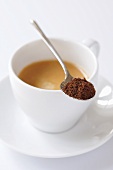 Spoonful of ground coffee on cup of espresso