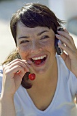 Young woman with a pair of cherries and a mobile phone