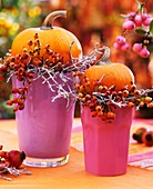 Pumpkins & rose hips on coloured beakers as table decoration