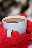 Hands in red gloves holding a cup of hot chocolate
