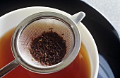 Cup of tea and tea strainer containing used tea leaves