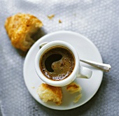 A cup of espresso with a croissant