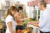 Drei junge Leute mit Gemüse und Kräutern in der Küche