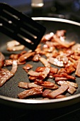 Frying strips of bacon in frying pan
