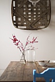 Geflochtener Korb an der Wand über Glasflasche mit Zweigen auf einem rustikalem Holztisch