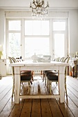 White crockery on white wooden table in front of tall, period windows