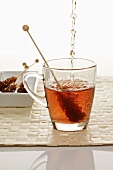 Pouring tea into glass cup with sugar swizzle stick