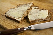 Slice of bread and butter, cut in half, with knife