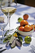 Frische Tomaten, Kräuter und Weissweinglas auf Tisch