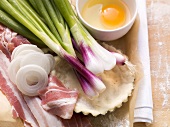 Ingredients for tarte flambée: spring onions, bacon slices, yeast dough, egg