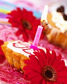Small cake with one candle and red gerberas