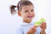 Little girl holding slice of bread with cucumber, quark and chives