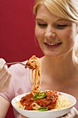 Blond woman eating spaghetti with tomato sauce