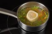 Clear broth with marrowbone and vegetables in pan