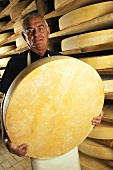 A man holding a wheel of cheese (Comte)