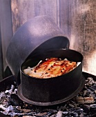 Stuffed breast of pork on scorzonera in stewpot on embers