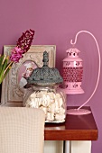 Pink lantern, glass jar of meringues and framed baby photo against lilac wall