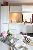 Set table with violet wine glasses in a modern fitted kitchen with white cupboards