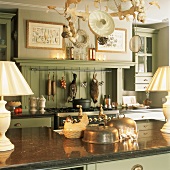 Landhausküche mit grüner Holzverkleidung und grünem Hängeschrank, Gasherd und alten Küchenutensilien auf polierter Arbeitsfläche