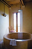 Round, unconventional stone bathtub with water falling from large rainfall shower head