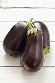 Three aubergines on a white painted wooden surface