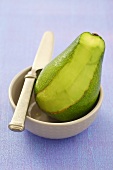 An avocado, sliced, in a bowl with a knife