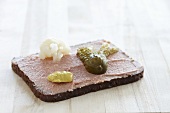Liver sausage spread on a slice of bread with mustard and a gherkin