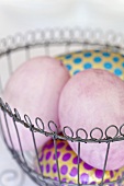 Coloured eggs, pink and spotted, in a wire basket
