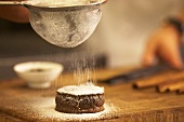 A mini chocolate cake being sprinkled with icing sugar