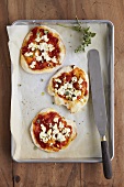 Small tomato and ricotta pizzas with oregano on baking tray