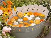 Marigolds, roses, grasses and floating candles in metal tub