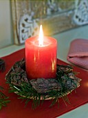 Red candle, Douglas fir and pieces of bark on saucer