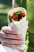 Hand holding chicken, bacon and spinach tortilla wrap