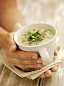 Hands holding a cup of creamed vegetable soup