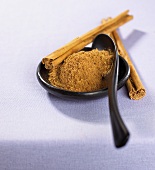 Ground cinnamon with spoon in a dish and cinnamon sticks