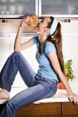 Young woman sitting on work tops biting into croissant