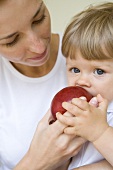 Small child biting into an apple her mother is holding