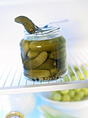 Pickled gherkin on fork and gherkin jar in fridge