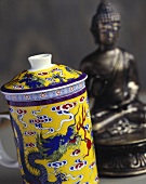 Decorated teacup with lid in front of statue of Buddha 
