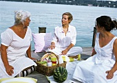 Drei Frauen sitzen um einen Picknickkorb auf dem Bootsteg