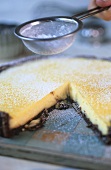 Sieving icing sugar over lemon tart with chocolate crust