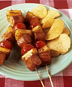 Grilled sausage & pineapple kebabs & potato crisps on plate