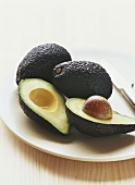 One halved and two whole avocados on a plate