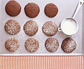 Chocolate biscuits on a baking tray with icing sugar